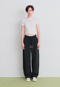 Cream cropped t-shirt, black drawstring pants, and white sneakers. The outfit features a relaxed fit and simple design.