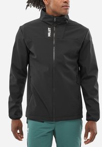 Veste softshell noire avec col haut, devant zippé et logo sur la poitrine. Dispose de manchettes élastiques et de deux poches latérales.