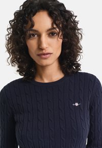 Maglione a maglia blu navy con motivo a trecce, scollatura rotonda e logo ricamato sottile sul petto. Tessuto morbido con polsini a costine.