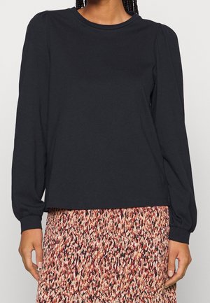 Femme portant un haut noir uni à manches longues bouffantes et une jupe multicolore à motifs.