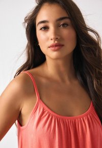 Koralinis liemenėliai su plonomis petnešėlėmis, laisvo silueto, su raukiniais ties kaklo linija, pagamintas iš minkštos, lygaus audinio.