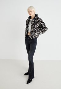 Leopard-print faux fur jacket with a zip-up front, black high-waisted jeans, and pointed black heels. Model poses against a plain background.
