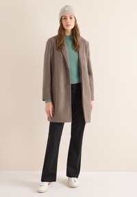 Abrigo de mezcla de lana gris con un corte relajado, botones de doble botonadura y grandes bolsillos, combinado con un suéter verde menta y pantalones negros.