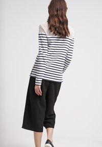 Randig långärmad topp i vit och marinblå, med spetsdetalj på axeln, matchad med svarta culotter. Tyget verkar mjukt och bekvämt.