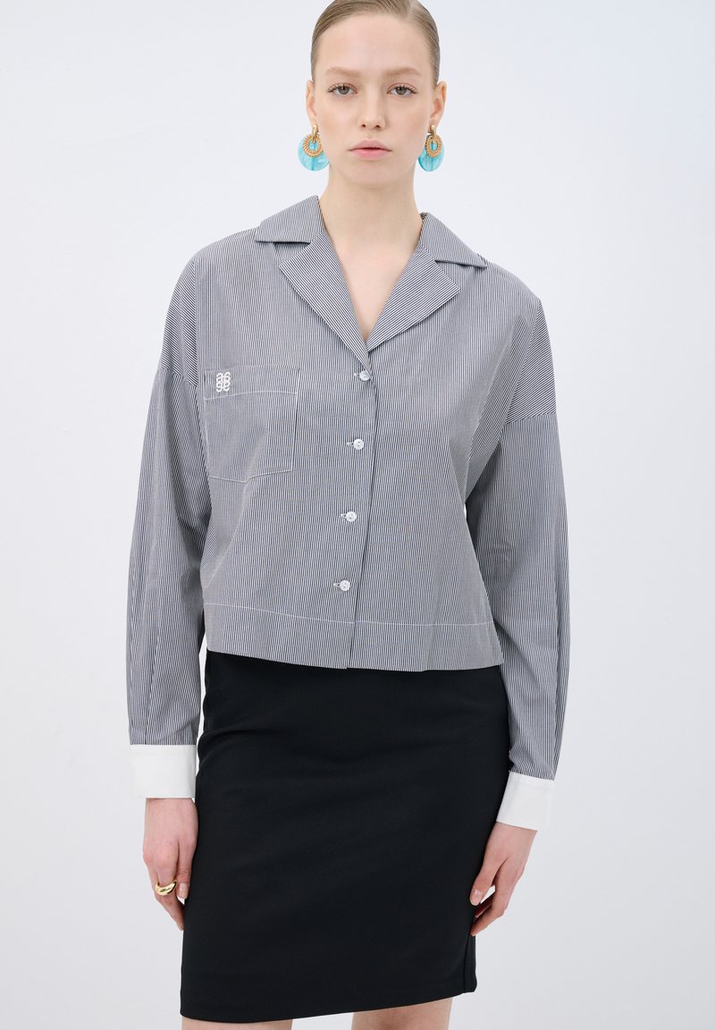 Rutig kort topp i grått med vit krage och manschetter, med en framficka och knappstängning. Matchad med en svart blyertskjol.