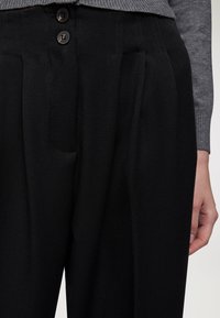 Pantaloni neri su misura con fronte piatto, dotati di due bottoni in vita, pieghe anteriori e una texture liscia.