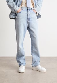 Lichtblauwe denimjeans met een ontspannen pasvorm, voorzien van een klassiek vijf-pocket ontwerp en een subtiele vervaagde textuur. Gemaakt in combinatie met witte sneakers.