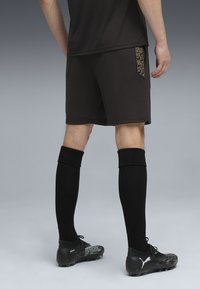 Sorte atletiske shorts med dekorative guld detaljer, kombineret med sorte knæ-høje sokker og sorte støvler med en struktureret design.