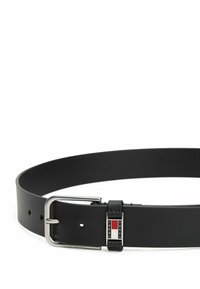 Zwarte leren riem met een zilveren metalen gesp en een logopatch met rode, witte en blauwe accenten. Gladde textuur en klassiek design.
