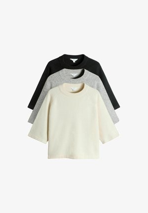 Tre kortærmede sweatre stablet: en sort, en grå og en cremefarvet. Blød tekstur, rund hals og raglanærmer. Minimalistisk design.