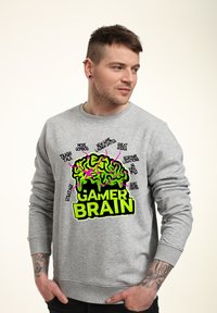 Felpa grigia con un vivace grafico neon verde e rosa "GAMER BRAIN" contenente testi relativi a strategie di gioco e funzioni.