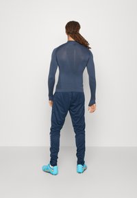 Haut de compression à manches longues bleu marine et joggeurs assortis avec une coupe fuselée. Chaussures de sport bleues. Texture lisse, design minimaliste, sans motifs.