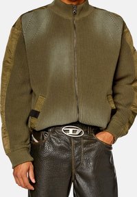 Olivgrön zip-up tröja med strukturerad stickning och släta ärmar; har sidofickor och en kontrasterande midjevaxtextur.