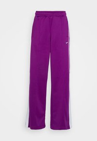 Purple sports pants with a wide-leg design, featuring a textured fabric, elastic waistband, and white side stripes. Nike logo on front.