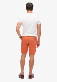 Pomarańczowe bawełniane szorty z dwiema tylnymi kieszeniami, pasem z klamrami oraz dołem kończącym się tuż nad kolanem. Noszone z białą koszulką.