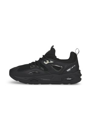 Baskets de sport Puma noires avec panneaux en mesh, fermeture à lacets, semelle épaisse, languette au talon et logo Puma blanc sur le côté.