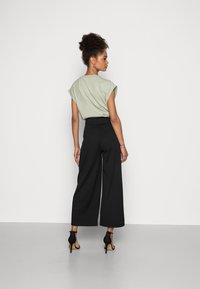 Haut vert à manches courtes associé à un pantalon large noir, avec une taille haute. Les détails de finition incluent des talons à bride de cheville.