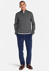 Grijze pullover met lange mouwen en rits, gecombineerd met marineblauwe corduroy broek. Donkerbruine schoenen met veters en een lichte hak.