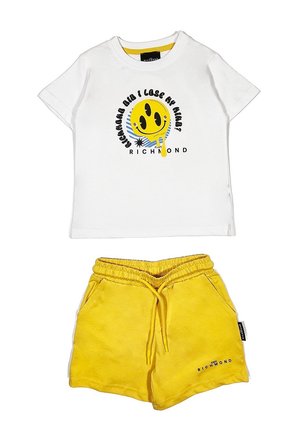 Maglietta bianca in cotone con una grafica di un smiley giallo e testo nero, abbinata a pantaloni corti gialli in cotone con vita elastica e tasche laterali.