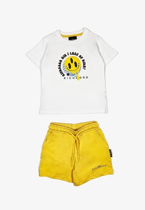 Maglietta bianca in cotone con una grafica di un smiley giallo e testo nero, abbinata a pantaloni corti gialli in cotone con vita elastica e tasche laterali.