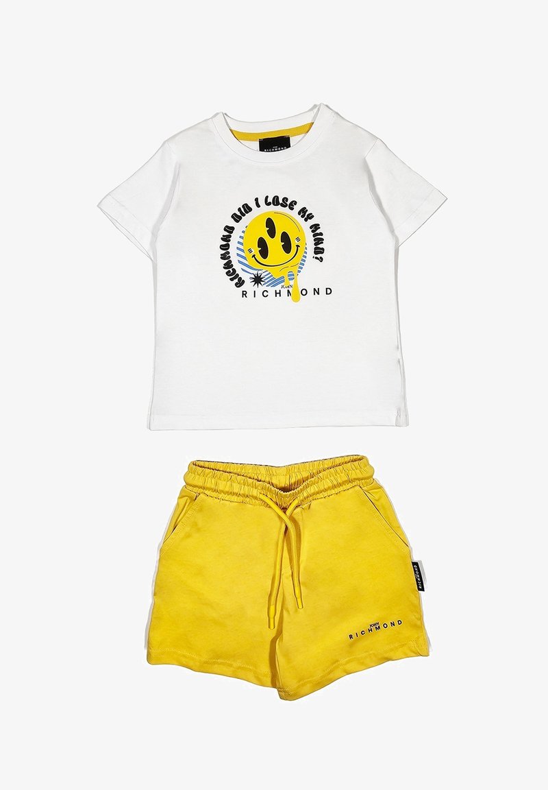 Maglietta bianca in cotone con una grafica di un smiley giallo e testo nero, abbinata a pantaloni corti gialli in cotone con vita elastica e tasche laterali.