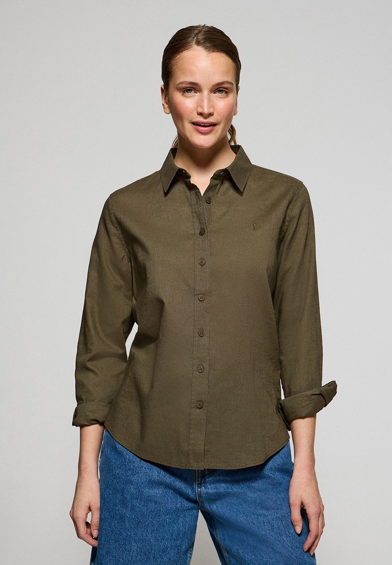 Olivgrön skjorta med knappar i strukturerad tyg, med klassisk krage, uppvikta ärmar och en liten logodetalj på bröstet.