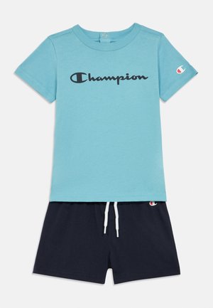 Light blue cotton t-shirt with "Champion" logo in black, paired with navy shorts featuring a drawstring and logo accent on the hem.