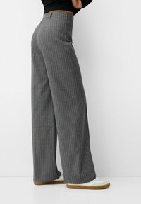 Pantalons larges à rayures gris en tissu texturé, dotés d'une taille mi-haute et associés à des baskets blanches.