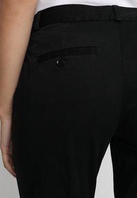 Pantalones negros a medida con un bolsillo trasero con cierre de botón, textura de tela suave y un diseño ajustado.