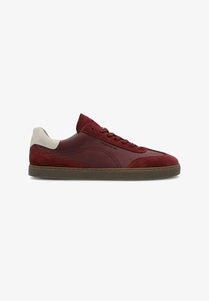 Zapatilla baja de cuero rojo con detalles en ante, lengüeta blanca en el talón, suela marrón y cierre de cordones, vista de lado sobre fondo blanco.