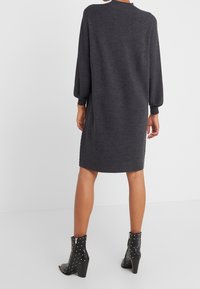 Robe en tricot gris charbon à manches longues et encolure ronde, avec des fentes latérales. Associée à des bottines noires cloutées.