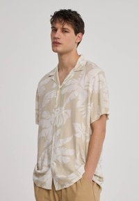 Camicia a maniche corte in beige chiaro con grandi motivi a foglia bianchi, dotata di chiusura a bottoni sul davanti e vestibilità comoda; realizzata in un tessuto morbido.
