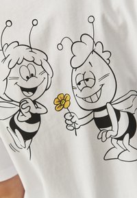 Hvid t-shirt med to tegneserie-bier med sorte striber, hvor den ene holder en gul blomst. Enkel stregkunst med legesyge udtryk.