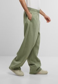 Pantalons de survêtement vert clair avec une coupe décontractée, taille élastique, poches latérales et une texture lisse, associés à des baskets couleur crème.