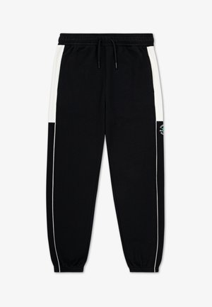 Pantalones de chándal negros con franjas laterales blancas, cintura elástica y puños en los tobillos. Incluyen un parche con logo en el muslo izquierdo. Hechos de tela suave.