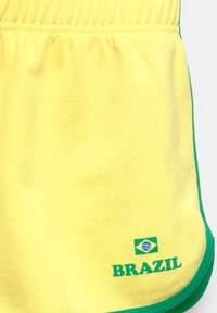 Gele sportieve shorts met een groene rand, voorzien van de tekst "BRAZILIË" en een klein logo van de Braziliaanse vlag nabij de onderzoom.