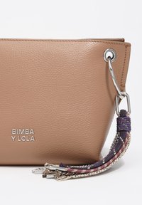 Torba na ramię w kolorze jasnobrązowym wykonana ze skóry z teksturowaną powierzchnią, srebrnymi elementami oraz wielokolorowym, plecionym frędzlem jako ozdobą. Logo umieszczone z przodu.