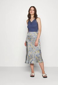 Mėlyna palaidinė be rankovių su nėrinių apdaila ir midi sijonas su gėlių ra�štu, kuriame geltonos ir baltos gėlės ant pilko fono; lengvos sandalai.