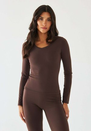 Brązowa bluzka z długim rękawem i dekoltem w kształcie litery V, wykonana z gładkiej, elastycznej tkaniny. Posiada dopasowany krój i minimalne detale przeszyć.