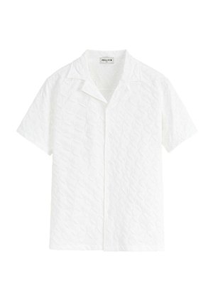 Chemise blanche à manches courtes avec un motif en losange, tissu texturé, col pointu et fermeture à boutons sur le devant.