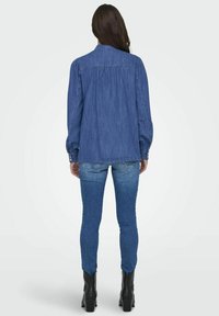 Denimskjorte i mellomblå, med en strukturert krage, lange ermer og ryggfold. Sammen med tettsittende blå jeans og svarte ankelstøvler.