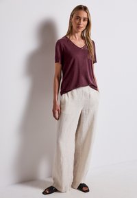 Camiseta de manga corta en burdeos con escote en V, combinada con pantalones de lino de pierna ancha en beige claro y sandalias negras tipo slide, con un corte holgado y bolsillos.