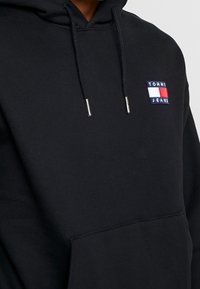 Felpa nera in misto cotone, con tasca a marsupio frontale e logo ricamato sul lato sinistro del petto in rosso, bianco e blu.