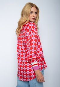 Langarmhemd in leuchtendem Rot mit einem geometrischen Muster in Pink und Weiß, gerippten Bündchen und einer lockeren Passform. Hergestellt aus glattem Stoff.