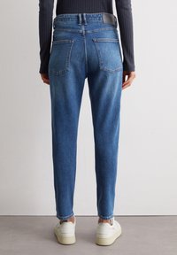 Jeans in denim blu aderenti con vita alta, design a cinque tasche e una piccola etichetta del marchio sul retro. Texture liscia con leggere sfumature.