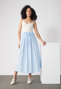 Jupe longue bleu clair avec une taille smockée, associée à un débardeur blanchi avec des dentelles. Accentuée par des talons ouverts beiges.