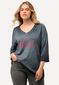 Maglietta grigia a maniche lunghe con scollatura a V, caratterizzata dalla scritta "Moin" in testo rosa; vestibilità rilassata con maniche arrotolate e orlo arrotondato.