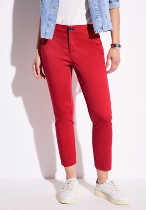 Pantaloni rossi slim-fit con una texture liscia, dotati di chiusura a bottone, tasche laterali e abbinati a sneaker bianche.