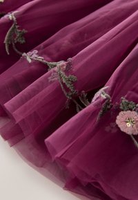 Tissu transparent violet profond avec des vignes vertes brodées et des motifs floraux roses, présenté en plis doux.