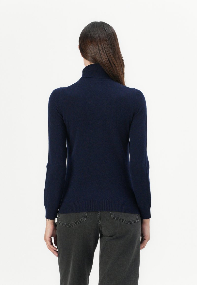 Dunkelblauer Rollkragenpullover, taillierte Passform, gerippte Bündchen und Saum, weicher Strickstoff, getragen mit dunkelgrauen Jeans, von hinten gezeigt.